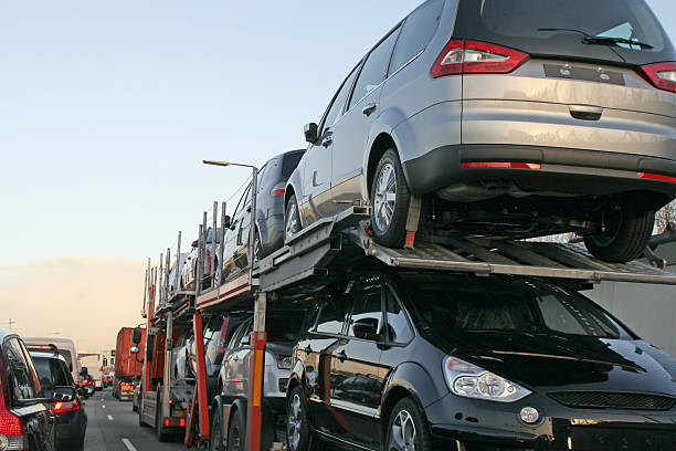 A car carrier truck transports multiple vehicles on a busy MI highway, surrounded by other cars and trucks in traffic—a typical scene for MI Car Shipping Lansing operations.
