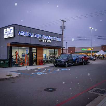 A small auto transport business with a sign reading American Auto Transport Pros. A black truck with cars on a trailer is parked outside—perfect for MI Car Shipping Lansing needs. Snow is falling. A Subway restaurant and tent are visible in the background.